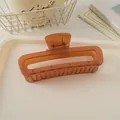 Gros plan d'une grande pince à cheveux carrée couleur ambre sur un plateau minimaliste - Marron Gelée