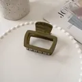 Detail of an olive green square claw clip with a glossy finish on a decorative tray - Dark Green