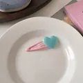 Detalle de una pinza para el cabello rosa con forma de corazón en una bandeja de cerámica - Clip Rosa con Corazón Azul
