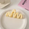 Detail einer cremefarbenen Haarklammer in Wellenform auf einer Keramikplatte - Wellenstil / Milchiges Gelb