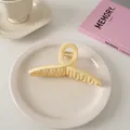 Detailansicht einer großen cremefarbenen Haarklammer auf einem weißen Teller mit Dekoration - Überkreuz-Stil / Milchiges Gelb