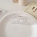 Detalle de una pinza de pelo cuadrada color crema con muelle dorado en plato cerámico - Transparente
