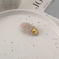Nahaufnahme der beigen Woll-Haarspange mit goldenem Emblem auf einem Keramikteller - Gebrochenes Weiß