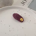 Close-up of a purple faux fur hair clip with a gold metal button on a ceramic plate - Purple