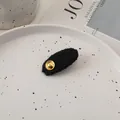 Close-up of black textured tweed oval hair clip with gold metal rivet on a stylish tray - Black