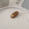 Close-up of brown plush wool hair clip with a vintage gold button on a ceramic plate - Brown