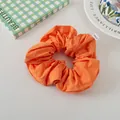 Detail of orange fabric scrunchie with white brand label on a minimalist aesthetic background - Bright Orange
