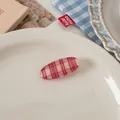 Close-up of a glossy red and white checkered oval hair clip on a vintage porcelain plate - 3# Fine Grid