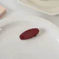 Vue détaillée d'une barrette ovale rouge foncé dans un plateau blanc en céramique lisse - Ovale court plein