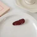 Détail d'une pince à cheveux ondulée bordeaux avec texture brillante sur plat - Goutte d'eau à rayures horizontales