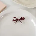 Détail d'une pince à cheveux nœud bordeaux avec perles sur une assiette blanche - Mince nœud papillon perlé