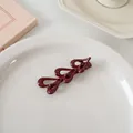Détail d'une pince à cheveux vintage rouge foncé brillante avec motifs en métal - Trois Cœurs