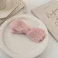 Détail macro d'une barrette noeud en laine rose à texture douce sur plateau céramique - Rose