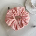 Detail of light pink satin scrunchie with soft sheen and Fndrea logo tag in glass tray - Pink
