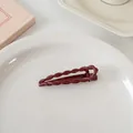 Detail einer burgunderroten Haarspange mit Drehmuster auf einem weißen Keramikteller - Gedrehter Wassertropfen