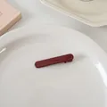 Vue détaillée d'une pince à cheveux rectangulaire rouge foncé sur une assiette - Court Droit