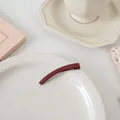 Détail de la barrette rouge foncé mat avec dents antidérapantes sur une assiette blanche - Pince droite courbée