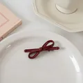 Gros plan d'une élégante pince à cheveux noeud rouge foncé sur une assiette en porcelaine - Nœud croisé