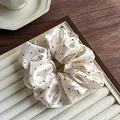 Dettaglio di un elastico scrunchie in satin crema a pois neri su un vassoio elegante - Beige Pois Neri