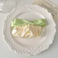 Detailaufnahme der cremefarbenen Satin-Haarspange mit grünem Band auf einem Porzellanteller - Grün