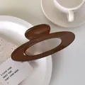 Detail of glossy dark brown hollow oval hair claw clip with smooth finish on a white plate - Coffee