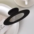 Minimalist black hollow oval hair claw clip with matte finish on a white ceramic plate - Matte Black