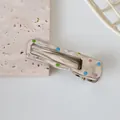 Macro view of silver metal hair clip with colorful dots on beige stone background - 6cm