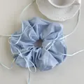 Macro shot of a light blue scrunchie with ribbons on a white background with a ceramic cup - Blue