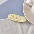 Cremefarbene ovale Haarspange mit bunten Sternen und Wellenrand auf weißem Stoff - Gelber Stern
