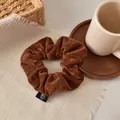 Detailed macro shot of brown velvet scrunchie texture with brand label and cafe props - Dark Coffee