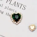 Dettaglio macro del cristallo smeraldo a forma di cuore da cucire con base dorata e strass - Base oro verde pavone