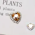 Dettaglio di toppa in cristallo a cuore ambra con bordo di strass e perni sul retro - Base K Bianco Champagne