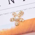 Exquise gouden bloem accessoire met glanzende strass steentjes en een witte parel - Goud