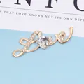 Detail der goldenen Love-Brosche mit herzförmigem Kristall und glitzernden Strasssteinen - Edelsteinstil