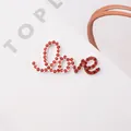 Macro shot of silver alloy Love script pendant with handset red rhinestones on white background - Red