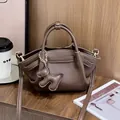 Detail der braunen Lederhandtasche mit Litschi-Muster und Teddybär-Anhänger auf Holztisch - Kaffeebraun / Mittel