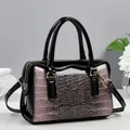 Détail du sac Boston avec texture croco rose, cuir verni noir et fermeture éclair dorée - Rose