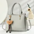 Close-up of grey leather Boston bag with gold buckle and cute plush bear keychain charm - Gray