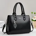 Elegant black leather handbag with silver logo and pearl leaf pendant on a studio background - Black