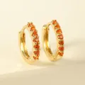 Macro shot of gold huggie earrings featuring a pavé setting with bright orange gemstones - Orange