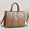 Brown leather handbag with gold oval buckle and detachable shoulder strap in a studio setting - Khaki