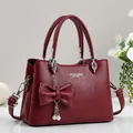 Detalle de bolso de mano rojo vino textura lichi con colgante de perlas y lazo decorativo - Rojo