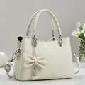 Detalle del bolso de piel con textura de lichi, lazo decorativo y colgante de perlas - Blanco Roto