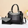 Close-up of black crocodile embossed patent leather bag with gold metal handle and clutch - Black