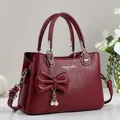 Burgundy faux leather tote bag with bow detail and pearl charm shown on white background - Red