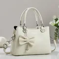 Detail of creamy white litchi texture handbag with large bow and pearl chain charm - Off White