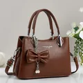 Detail of dark brown lychee pattern leather bag with decorative bow and metal chain charm - Earthy Yellow