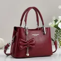 Detail of burgundy lychee leather handbag with decorative bow and pearl pendant charm - Red