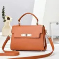 Classic tan textured leather handbag with gold hardware and top handle shown on podium - Khaki/Earth Yellow