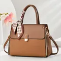 Detail der Macaron-Handtasche mit Prägung, Goldbeschlägen und einem Seidenschal mit Hahnentritt - Erdgelb